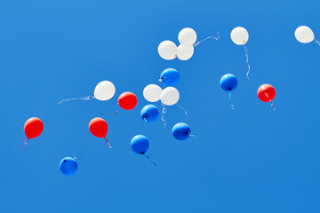 Multicolored helium balloons flying up in the blue sky