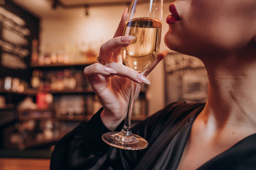 a girl in a black dress with red lips held a glass of champagne close to her lips