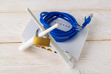 Padlock on Wi-Fi wireless router antennas and disconnected blue network cable on a white wooden...