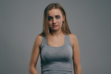 Obraz premium Blonde girl with bruises on her face posing against gray studio background. Domestic violence, abuse. Depression, despair. Close-up, copy space.