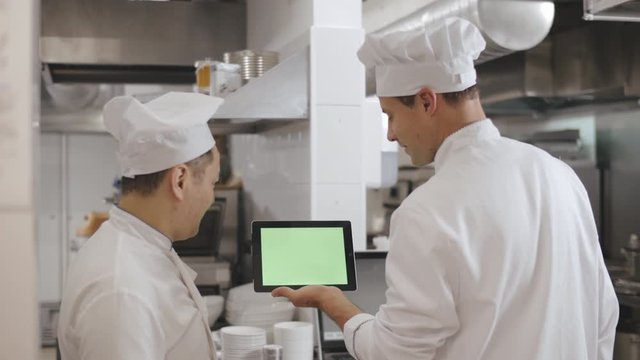 Cooks creating new recipe using digital tablet standing in industrial kitchen