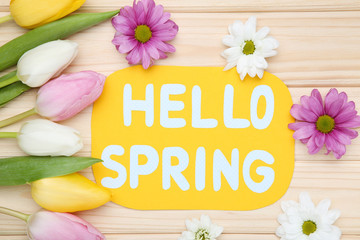 Fototapeta premium Tulip, chrysanthemum flowers with text Hello Spring on brown wooden table
