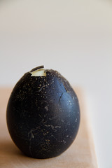 Boiled chicken egg painted in a dark color, slightly cleaned on a blurry background