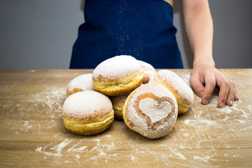 The cook sprinkles icing sugar on fresh donuts. Do-it-yourself donut cooking.