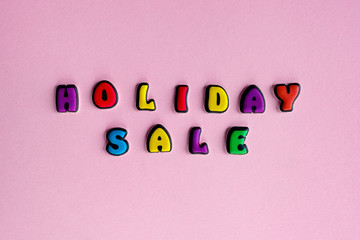 Inscription Holiday Sale composed of colored letters on a pink background. Discount and advertisement. Seasonal sale in stores. The photo for a banner or poster on the site and on social networks. 