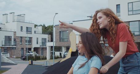 Pretty ginger girl riding her best friend in wheelchair outdoor. Attractive smiling invalid girl...