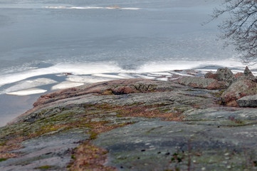 The rocky shore of a large lake in early spring, large stones and melting ice near the shore on a cloudy spring day.
