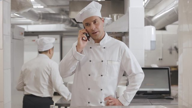 Happy chef cook standing in commercial kitchen and talking on phone