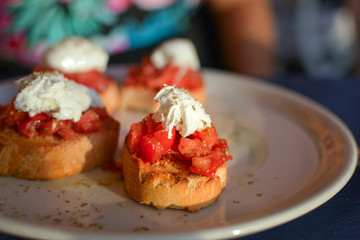 A plate of bruschetta with tomatoes on the baked bread and a spoonful of whipped ricotta cheese on top from a sidewalk cafe in Vernazza Italy