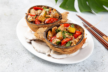 Hawaiian pinapple chicken in natural coconut shell plates on white background