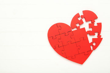 Broken puzzle heart on white wooden table