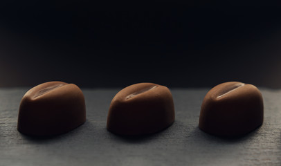 Obraz na płótnie Canvas Three coffee bean shape chocolate on dark background