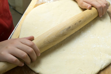 Photo of the hands of a man who rolls the dough with a rolling pin.