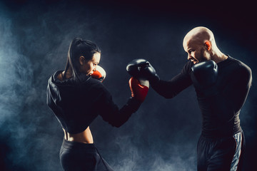 Woman exercising with trainer at boxing and self defense lesson, studio, smoke on background. Female and male fight