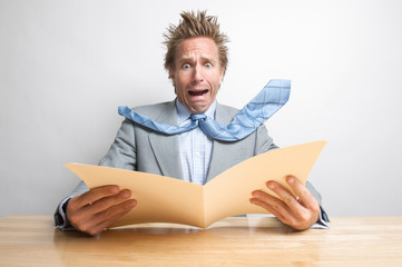 Shocked office worker screaming at the contents of a file folder open on his desk 