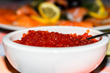 red caviar in a white saucer on a table against a background of red fish and lemon