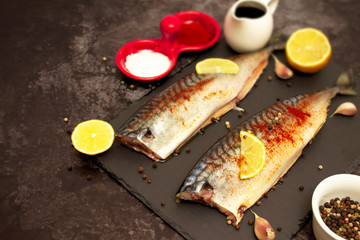 Raw mackerel lies pickled with lemon and paprika on a slate board, next to spices and soy sauce....