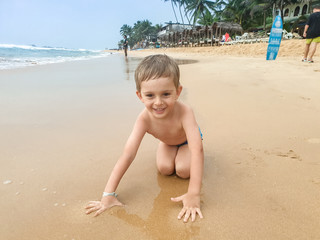 Portrait of smiling little boy sitting on the wet sand at ocean beach