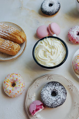 Eclairs, strawberry and lavender macarons, sweet donuts with cup of capuccino and marshmallow on white marble table