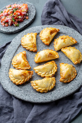 Different little cocktail EMPANADAS on stone plate with tomato sauce and guacamole . Gray background. Latin American and Spanish tipical food