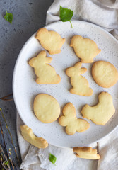 Easter cookies on a ceramic plate with napkin, grey stone background. Homemade butter and sugar cookies.