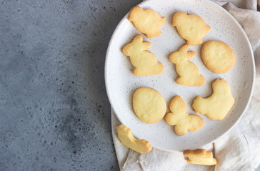 Easter cookies on a ceramic plate with napkin, grey stone background. Homemade butter and sugar cookies.