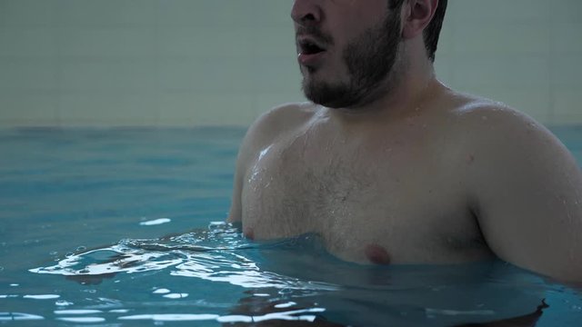 handsome bearded guy takes deep breathe and dives into blue swimming pool water slow motion close view
