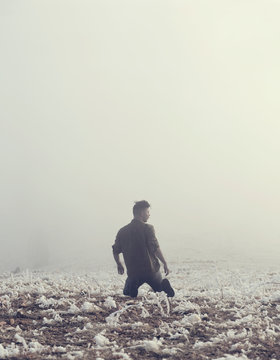 Man kneels in foggy winter field, artistic conceptual image 