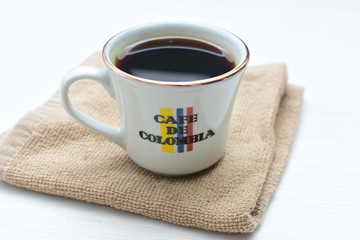 Traditional cup of Colombian coffee with coffee beans on wooden background