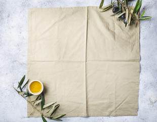Food background with linen napkin, olive tree branch, olive oil on concrete background