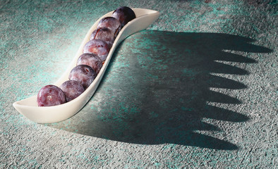 Frozen fresh plum in a curved white dish casts a hard shadow. Copy space..