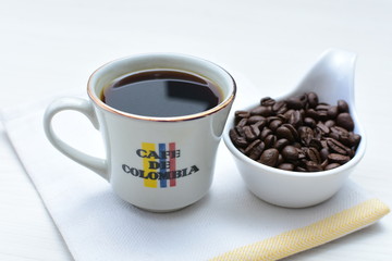 Traditional cup of Colombian coffee with coffee beans on wooden background