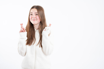 Fototapeta premium Pleased cheerful brunette woman puts all efforts in wishing good luck, crosses fingers, has faith for better, dressed in oversized hoodie, isolated over pink background