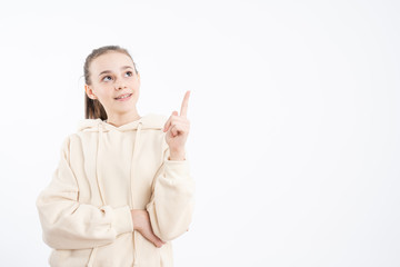 Overjoyed young woman points aside with fore finger, isolated over white background, dressed in casual clothing