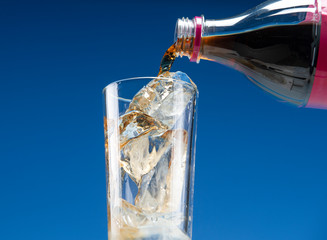 Carbonated drink is poured from a plastic bottle into a glass with ice