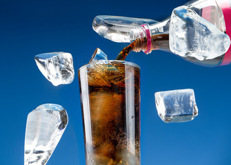Carbonated drink is poured from a plastic bottle into a glass with ice