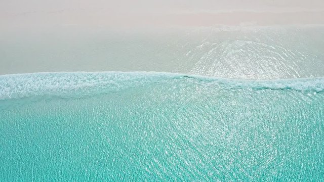 Aerial shot of turquoise water and waves rolling in from bottom of frame onto the sand of Australia's whitest beach - Lucky Bay