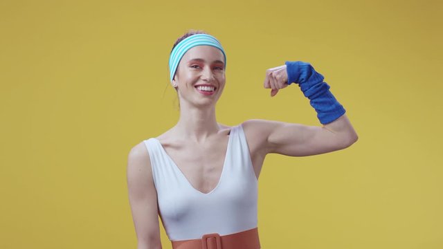 Happy confident sports woman athlete showing her biceps and boasting of her strong muscles smile cheerful at camera isolated on yellow. Expressions. Boxing champion.