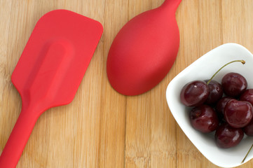 Red Spoon with Bowl of Cherries on Wood Background