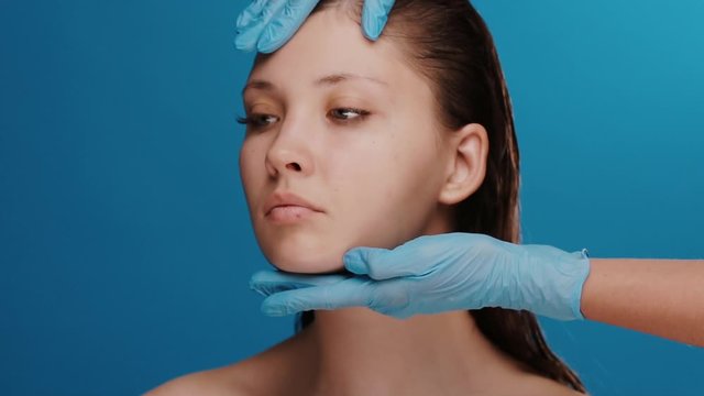 cosmetic surgeon examing female head and face before operation on blue background