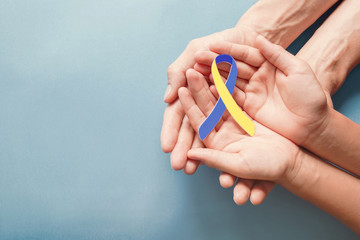 Adult and child hands holding blue and yellow ribbon shaped paper, Down syndrome awareness , World down syndrome day