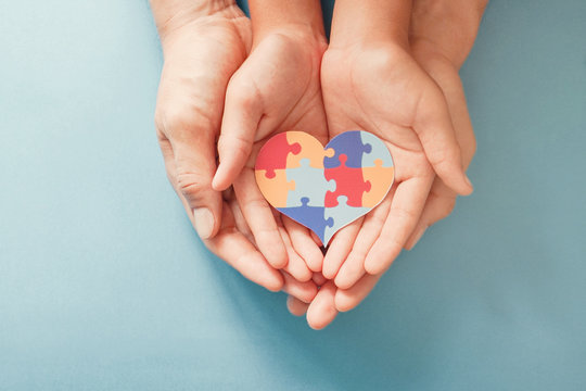 Adult and chiild hands holding jigsaw puzzle heart shape, Autism awareness, Autism spectrum family support concept, World Autism Awareness Day
