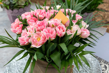 Large bouquet of pink tulips with palm leaves and paper with copy space