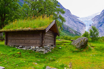 Traditional houses with green grass on the roof against the background of the Briksdalsbreen (Briksdal) glacier which is the sleeve of large Jostedalsbreen glacier. Norway.