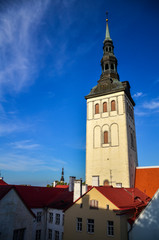 Fototapeta na wymiar St Nicholas Church (Estonian: Niguliste kirik) and red roofs in Tallinn, Estonia. The white tower is topped by a black spire, against a blue sky.