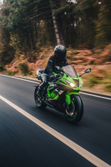 Fototapeta na wymiar Biker biking a green motorcycle in the forest road