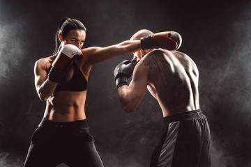 Fototapeta na wymiar Woman exercising with trainer at boxing and self defense lesson, studio, smoke on background. Female and male fight