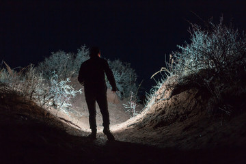 Man explores dark landscape at night using flashlight, artistic photo