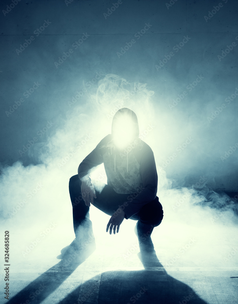 Wall mural Man squatting in empty room with smoke and light coming from his hooded face