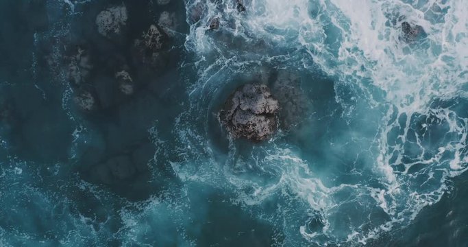Aerial view of powerful waves breaking over a rocky coastline at dusk, moody nature backgrounds